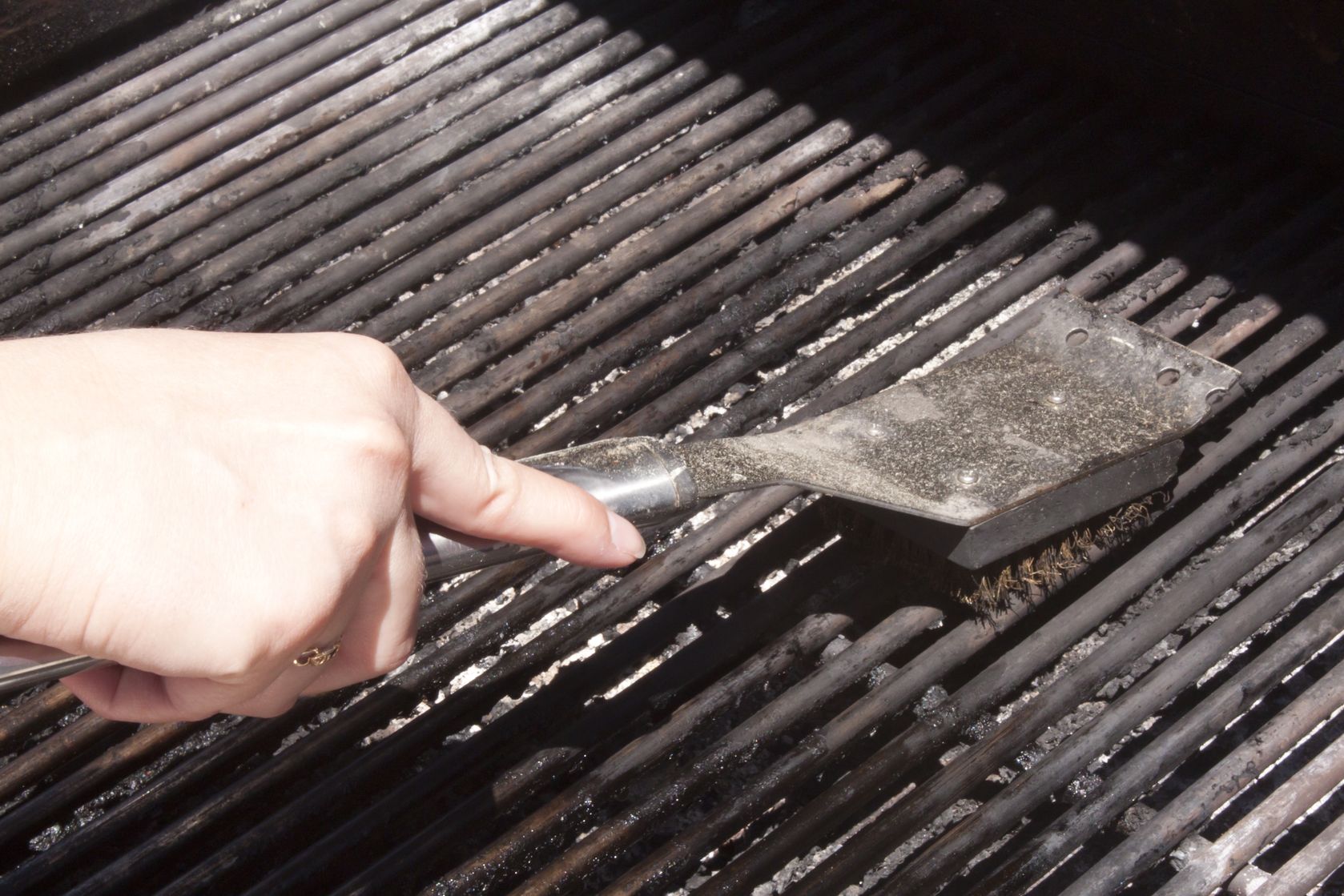 Person scrubbing BBQ grill grates with a brush.