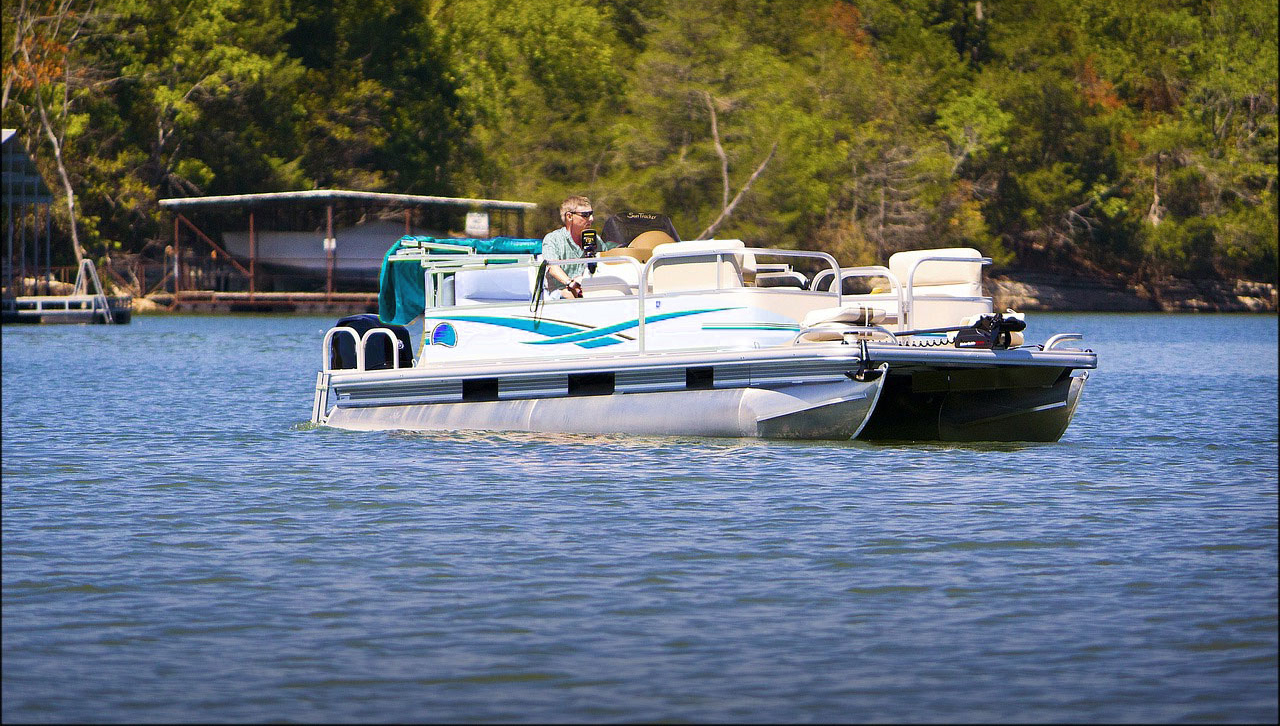 Person steering a pontoon boat in water.